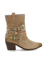 Bota corta de cuero gamuza color beige, con taco de madera y punta fina. Presenta tres tiras con hebillas metálicas plateadas y tachas pequeñas alrededor del tobillo.
