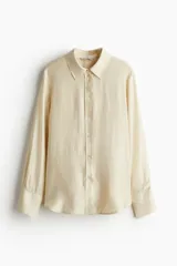 Camisa color crema de manga larga con puños abotonados, cuello clásico, cierre frontal con botones y bajo redondeado.