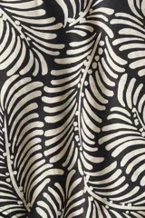 Blusa oversized con estampado de hojas en blanco y negro, cuello con volados y lazos, mangas largas raglán con puños elásticos y bajo redondeado.