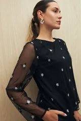 Blusa negra de tul bordado con pequeñas lentejuelas y mangas largas transparentes.