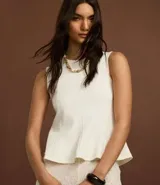 Blusa sin mangas color blanco, confeccionada en punto roma, con cuello redondo y corte peplum.