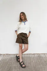 Buzo blanco de algodón con cuello polo con botones, mangas largas con puños acanalados a rayas en tonos marrón y celeste.