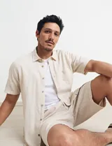 Bermuda de lino color beige, con bolsillos laterales y traseros. Cierre frontal con botón y cremallera.