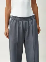 Pantalón deportivo color borgoña, de corte ancho y cintura elástica. Presenta una franja blanca vertical a lo largo de la pierna.