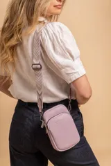 Bandolera pequeña tipo 'phone bag' de símil cuero color rosado pálido, con cierre de cremallera y correa ancha de tela con diseño de chevron en tonos claros.