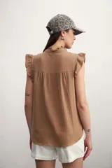 Camisa color amarillo pálido con cuello mao, sin mangas, con volados en los hombros y en el frente.