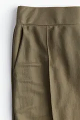 Pantalón de vestir color verde oliva, de punto con pinzas, tiro alto con cintura elástica, bolsillos al bies y piernas amplias con raya adelante.