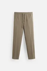 Pantalón color arena de corte recto, confeccionado en tejido elástico. Cuenta con cintura elástica ajustable con cordón, bolsillos laterales y bolsillos de vivo en la parte trasera.