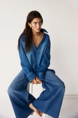 Camisa de denim azul con cuello abierto y canesú con pliegue de caja en la espalda. Modelo de corte holgado con hombros caídos y mangas largas con botones a presión en los puños. Bajo recto, algo más largo atrás, con aberturas laterales.