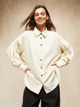 Camisa de pana fina color crudo, con cuello camisero, botones negros y mangas largas abullonadas con puños.