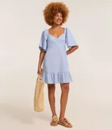 Vestido corto evasê de viscolino color crudo, con escote en V, mangas cortas amplias, recorte cut-out en los laterales de la cintura y volado en el ruedo.