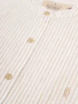 Camisa de manga larga con cuello mao, confeccionada en tejido de lino rayado en tonos gris y blanco. Cierre frontal con botones.