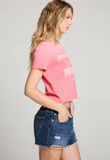 Camiseta corta color rosa con estampado frontal de la frase "Here Comes The Sun" y siluetas de personas caminando.