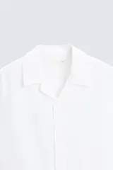 Camisa color marrón oscuro de corte relaxed fit, confeccionada en tejido de lino. Tiene cuello bowling, manga corta, bajo con aberturas laterales y cierre frontal de botonadura.