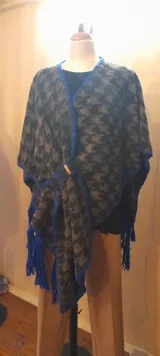 Ruana artesanal con diseño de patchwork en la espalda, terminación de pespuntes y crochet en lana con flecos azules.