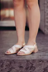 Sandalias bajas color beige con tiras cruzadas y elástico dorado en el talón.