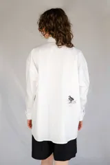 Camisa blanca de algodón con cuello con lengüeta y botón labrado, manga larga con puños y botones, corte oversize y estampado de aves en el delantero.