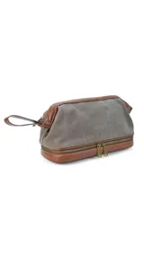 Neceser verde de tela canvas combinado con símil cuero marrón. Tiene apertura superior con cierre metálico estructural, doble bolsillo interno (uno con cierre y otro abierto con división) y base con cierre que actúa como bolsillo extra.