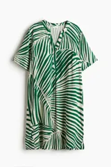 Vestido túnica a la rodilla en tejido liviano de viscosa con cuello mao y abertura en V. Modelo de corte holgado con hombros levemente caídos, mangas cortas y bajo recto con tajos laterales. Parte posterior algo más larga. Sin forrar. Estampado con hojas de palmera en verde y blanco.