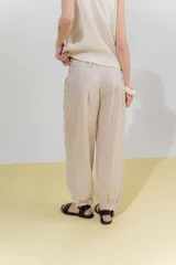 Pantalón de lino color marrón, con corte tipo barrel, tiro medio, pretina ancha con doble abotonadura, bolsillos laterales y pinzas en el frente. Ruedo con presilla permitiendo usarlo recto o fruncido al tobillo.