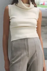 Pantalón tobillero color gris claro, de tiro alto, con bolsillos delanteros de vivo y cierre frontal con cremallera, botón interior y gancho metálico.