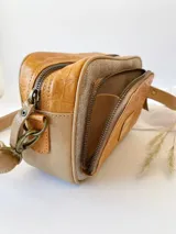 Bandolera de cuero color tostado con textura tipo cocodrilo en la parte frontal. Tiene correa larga regulable y cierre con cremallera.