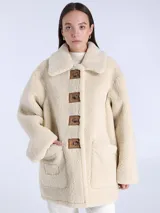 Chaqueta reversible de piel de oveja color crema con botones cuadrados de cuero marrón y bolsillos delanteros.