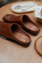 Mules de cuero negro con punta cuadrada y detalle de tachas plateadas en el borde superior.