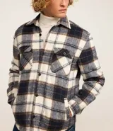 Campera trucker masculina de franela a cuadros en tonos blanco, negro y gris, con cuello inglés, abotonado delantero, bolsillos con solapa en el pecho y bolsillos laterales. Interior forrado en sherpa.