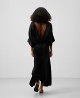 Vestido largo negro de mujer con manga japonesa, cuello caja en delantero y escote en espalda con nudo. Ajuste en cadera con godets y bajo asimétrico.