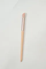 Brocha de maquillaje con mango largo y cabezal suave, ideal para difuminar sombras.