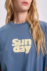 Remera celeste de corte amplio con estampa amarilla con la palabra 'Sunday'.