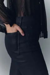 Pantalón jean de tiro medio, confeccionado en denim azul con coating negro que le da apariencia de cuero. Es ajustado en la cintura y levemente acampanado desde la cadera al ruedo.