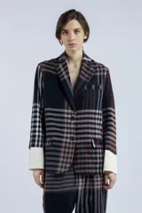 Blazer con estampado a cuadros en tonos marrones y negros, de corte recto y silueta relajada. Presenta solapas clásicas, cierre frontal con botones y bolsillos con tapa. Mangas largas con puños blancos.