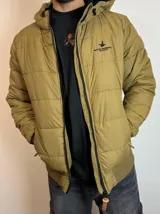 Campera inflada color ocre con capucha, cierre frontal con cremallera y logo de la marca bordado en el pecho.