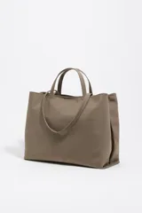 Bolso shopper grande de nylon negro, con estructura blanda, doble asa de mano y correa larga ajustable para llevar al hombro. Presenta un logo metálico con el texto "BIMBA Y LOLA" en la parte frontal inferior.