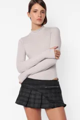 Minifalda gris con estampado de cuadros escoceses, cintura ancha, tablas en la parte inferior y cierre metálico lateral. Incluye sobrefalda desmontable con bolsillo.