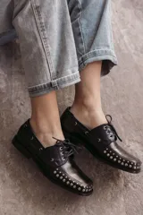 Mocasín de cuero negro con cordones y tachas metálicas en la puntera.