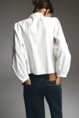 Camisa blanca de cuello subido y manga larga, con detalle de entredós combinados a tono y cierre frontal con botones.