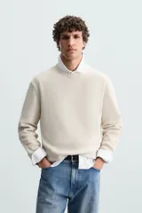 Jersey color crudo tejido en hilatura de algodón, con cuello redondo, manga larga y acabados en rib.