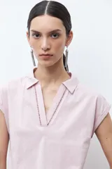 Remera de manga corta color rosa pálido, con cuello polo y escote en V con detalle de bordado en el borde.