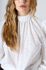 Blusa blanca de broderie con cuello alto, mangas largas abullonadas y puños elásticos.