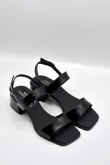 Sandalias de cuero color beige con taco cuadrado y tira ancha sobre los dedos. Presenta pulsera al tobillo con hebilla dorada.