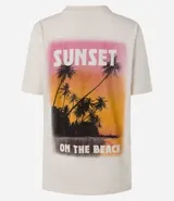 Remera alargada de algodón color crema con estampa de palmeras y atardecer en la playa.