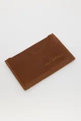 Tarjetero de cuero marrón con costuras en los bordes y logo de la marca SierraMora grabado en el frente. Tiene ranuras para tarjetas en ambos lados.