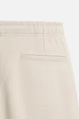 Pantalón de jogging color beige confeccionado en tejido de mezcla de algodón. Cuenta con cintura elástica ajustable con cordón, bolsillos frontales y traseros.