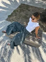 Pantalón de jean ancho, color verde oscuro o gris verdoso, de tiro alto con pliegues frontales y corte extremadamente holgado.