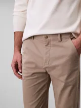 Pantalón chino de corte slim color beige, confeccionado en algodón y elastano. Presenta cierre con cremallera y botón, diseño clásico de cuatro bolsillos y logo de Calvin Klein bordado en la parte posterior.