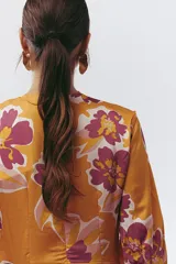 Vestido largo color naranja con estampado floral en tonos fucsia y blanco, escote en V y mangas largas.