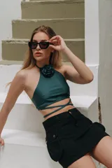 Top de bikini verde esmeralda con detalle de flor en el cuello y tiras cruzadas en la cintura.